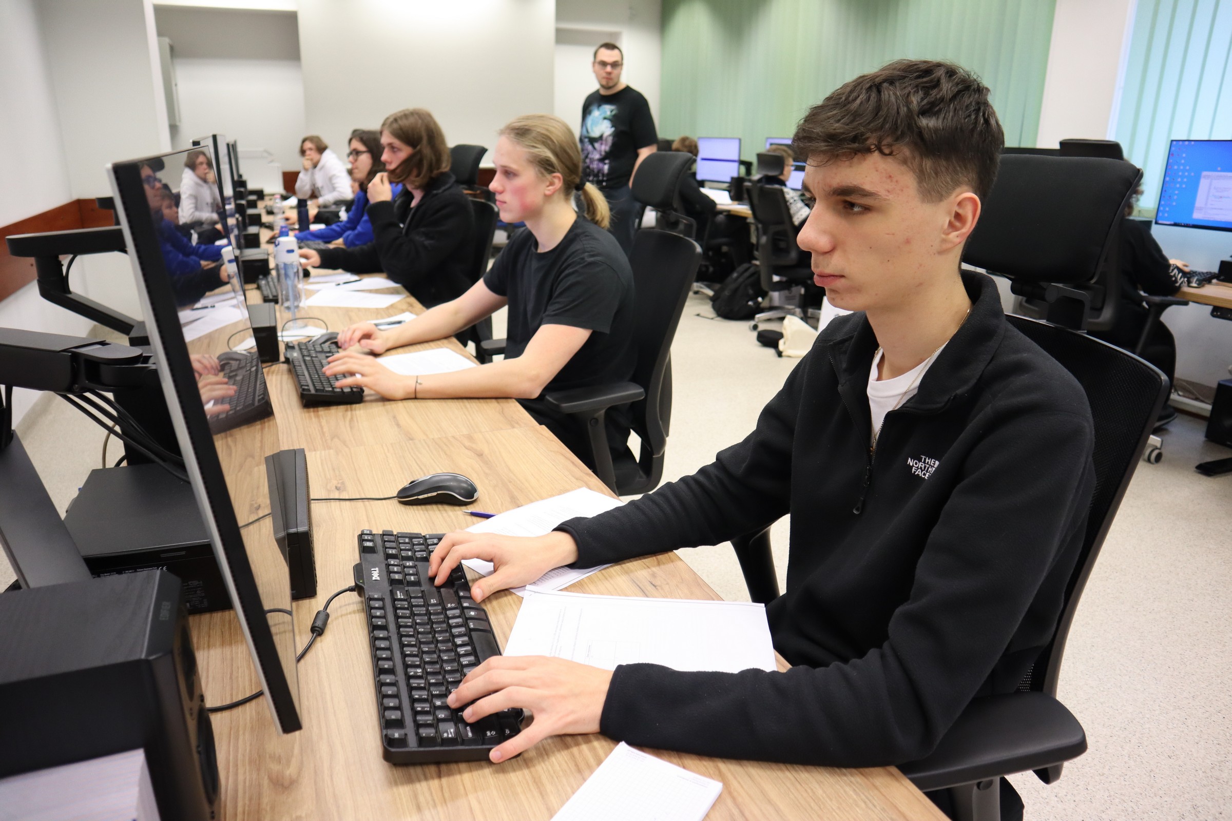 Uczestnicy konkursu ze skupieniem pracują przy komputerach rozwiązując zadania